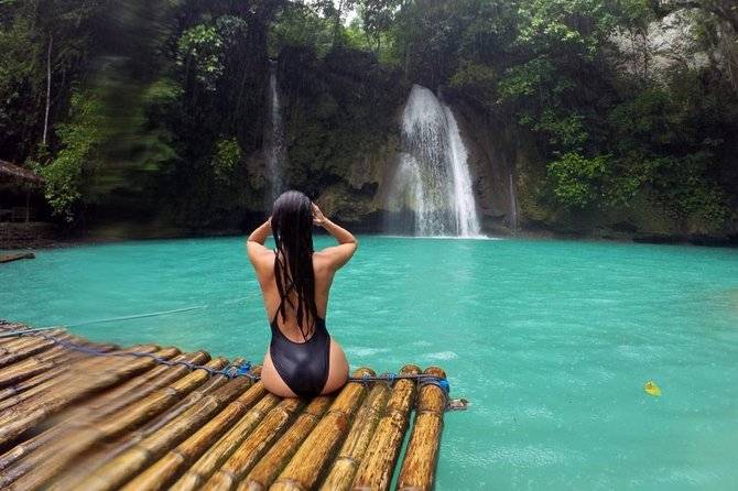 woman sitting on bamboo raft in front of waterfall